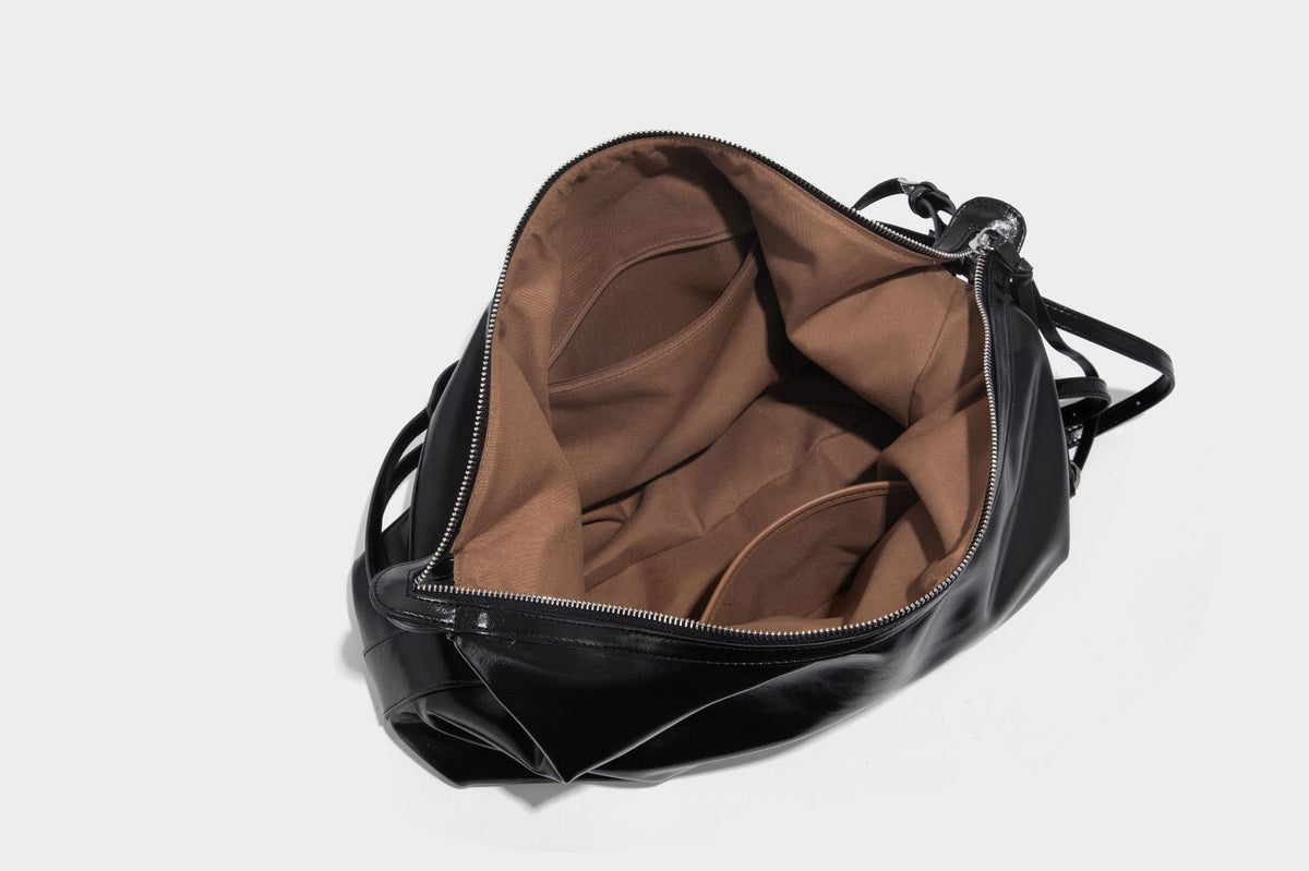Glossy black slouchy hobo shoulder bag with zip closure, silver-tone ring hardware, and adjustable crossbody strap, detail