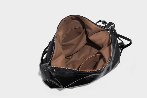 Glossy black slouchy hobo shoulder bag with zip closure, silver-tone ring hardware, and adjustable crossbody strap, detail