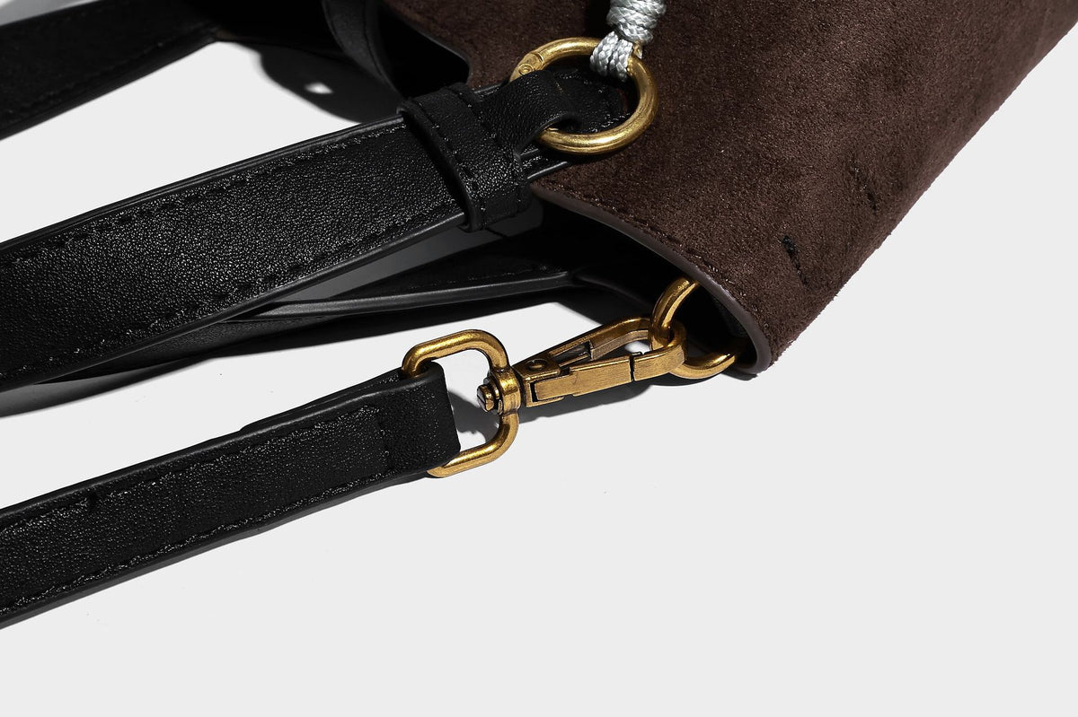 Small structured trapezoid tote bag in matte suede-look finish with black contrast trim, gold-tone front clasp, tassel charm