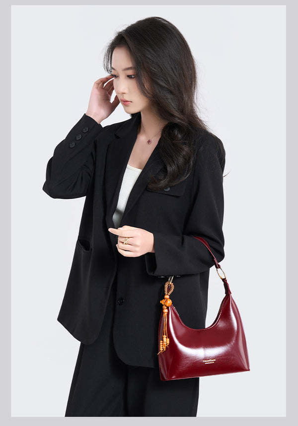 Glossy crescent hobo shoulder bag in deep burgundy with beaded wood tassel charm and gold-tone ring hardware, detail view 8