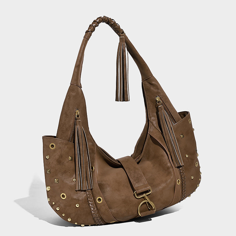 Slouchy crescent hobo bag in matte brown suede-like finish with gold-tone studs, grommets, braided top handle, tassel side