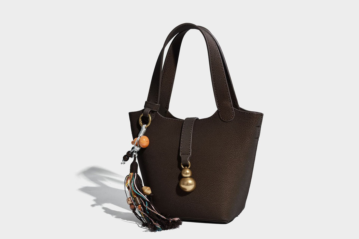 Kleine matte Beuteltasche mit genarbter Oberfläche, antikgoldfarbenen Ringbeschlägen, Perlen- und Quastenanhänger, kurzen Tragegriffen oben und