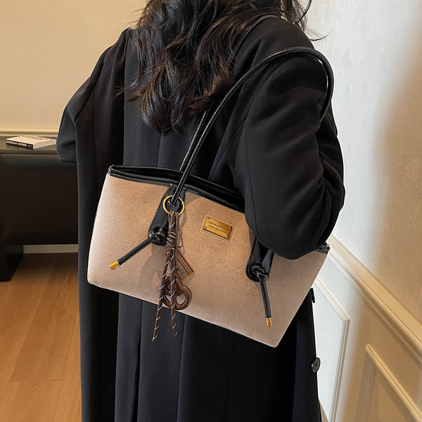 Structured suede-finish tote bag with glossy black leather-look trim, dual top handles, and decorative hanging charm in