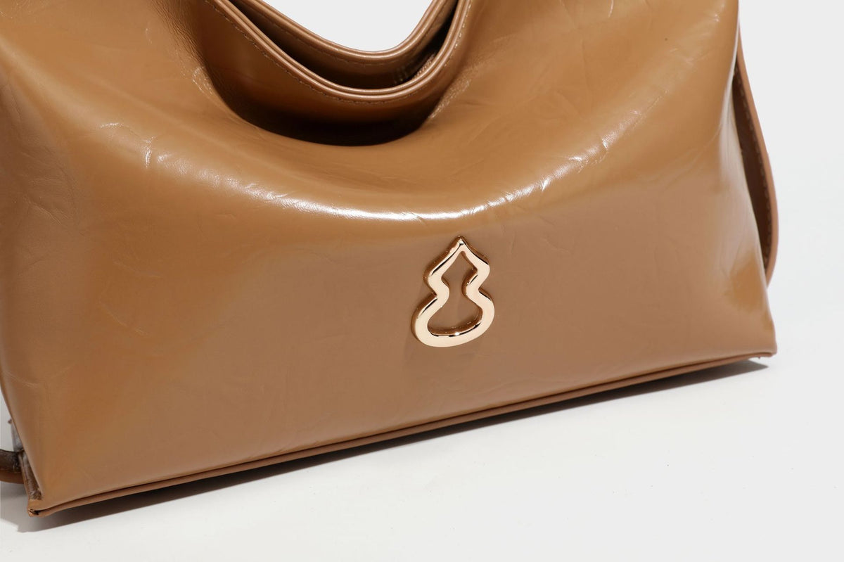 Lässig fallende Hobo-Schultertasche mit offenem Oberteil aus glänzender, karamellbrauner Lederoptik, mit Logo-Beschlägen in Goldoptik und langem, verstellbarem