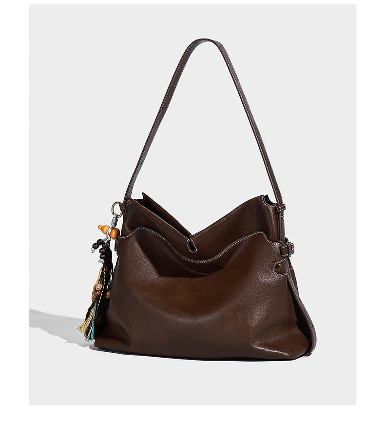 Large slouchy leather-look hobo tote bag with open top, adjustable shoulder strap, and colorful tassel bead charm, detail