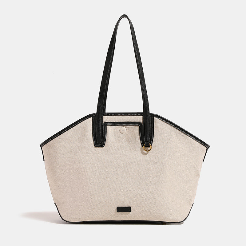 Cream canvas trapezoid tote bag with black leather-look trim, dual shoulder straps, and gold-tone ring hardware, front view