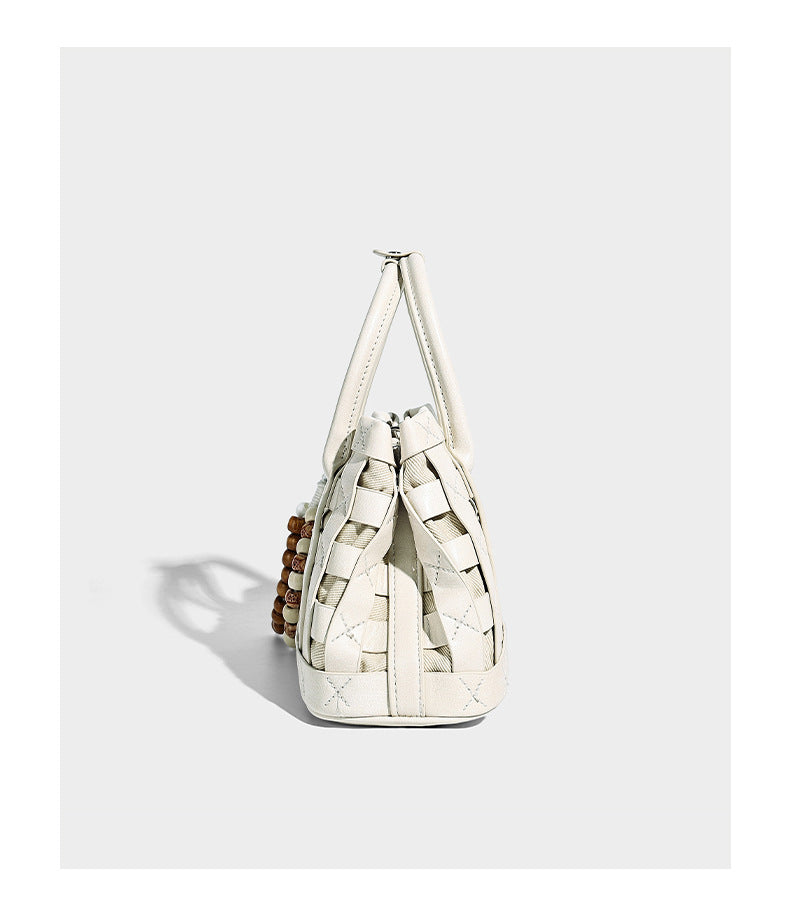 Small structured woven satchel tote with rounded top handles, silver-tone ring hardware, and bead tassel charm, detail view