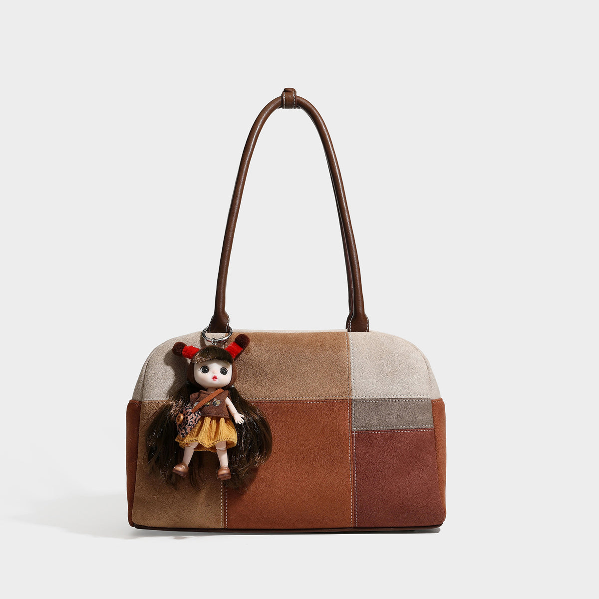 Boxy patchwork suede-look shoulder tote in tan, beige, rust, and brown panels with double brown straps and hanging doll