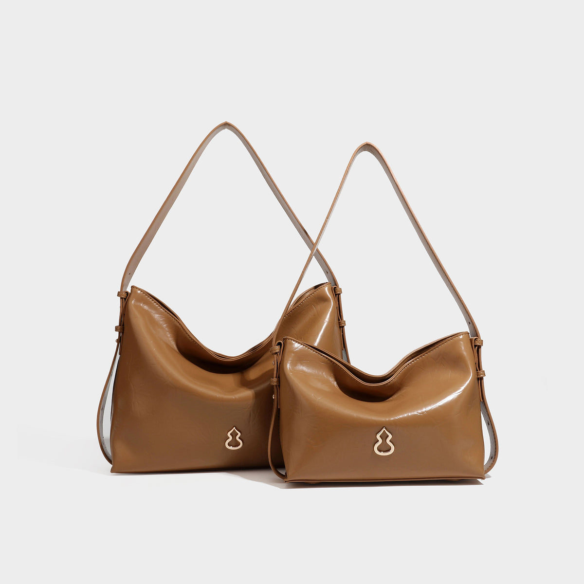 Lässig fallende Hobo-Schultertasche mit offenem Oberteil aus glänzender, karamellbrauner Lederoptik, mit Logo-Beschlägen in Goldoptik und langem, verstellbarem