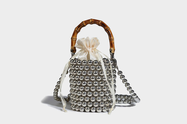 Small cylindrical bucket bag with glossy faux-pearl bead exterior, bamboo arched top handle, satin drawstring closure, and