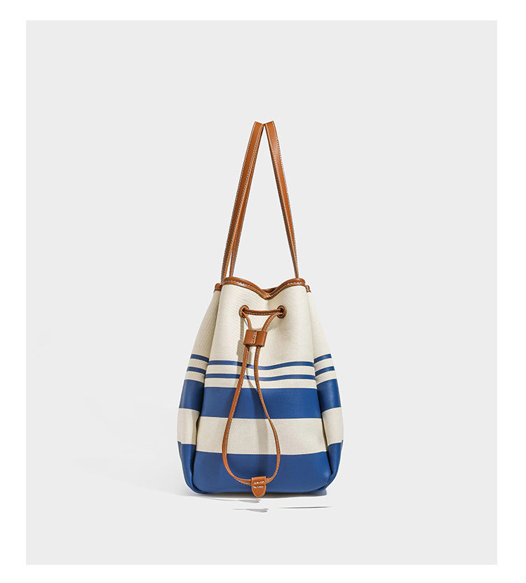 Large cream and navy striped canvas bucket tote bag with tan leather-look trim, drawstring closure, and double shoulder