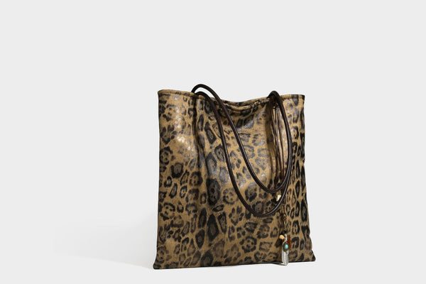 Large leopard print shoulder tote bag in tan and brown with slim dark straps and dangling beaded charm hardware, detail view