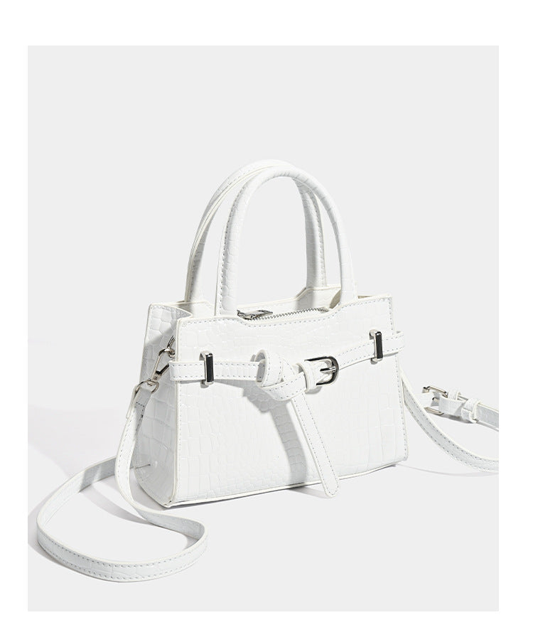 Small structured trapezoid mini top-handle bag with front belt-knot buckle detail and glossy leather-look finish, detail view