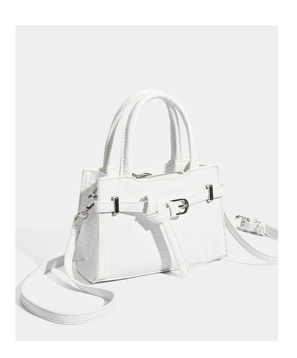 Small structured trapezoid mini top-handle bag with front belt-knot buckle detail and glossy leather-look finish, detail view