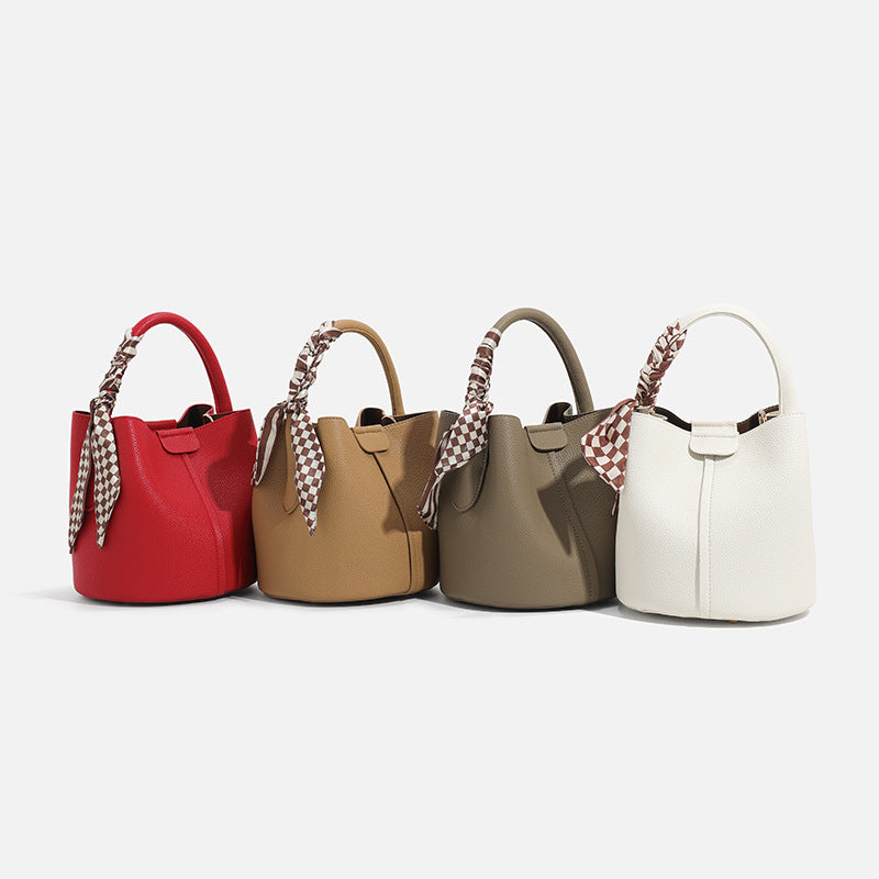 Pebbled leather-look bucket bag with checkered scarf-wrapped top handle, flap tab closure, gold-tone hardware, and matching