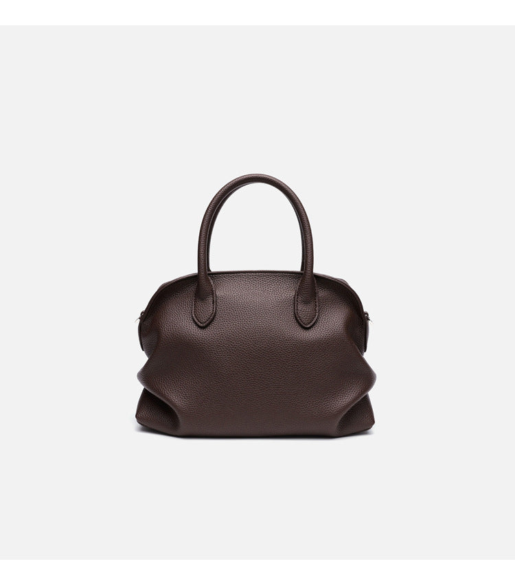Rounded dome shell handbag in pebbled leather-look finish with twin top handles, zip closure, decorative horse charm, and