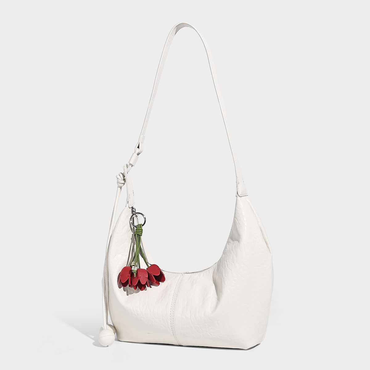 Slouchy crescent half-moon shoulder bag in pink pebbled textured finish with floral charm and knotted side detail, detail