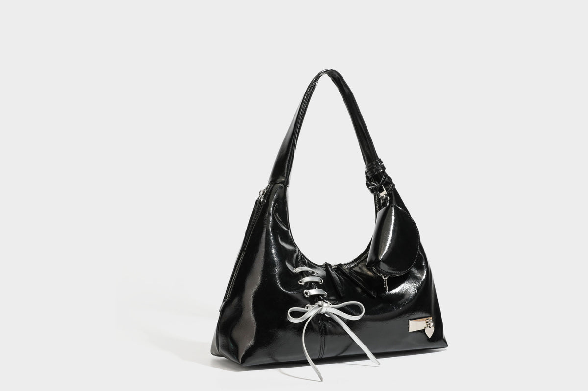 Weich fallende Hobo-Schultertasche in glänzender Lederoptik mit silberfarbenen Ösen zum Schnüren und Schleifenband auf der Vorderseite, Detailansicht