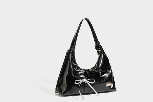 Weich fallende Hobo-Schultertasche in glänzender Lederoptik mit silberfarbenen Ösen zum Schnüren und Schleifenband auf der Vorderseite, Detailansicht