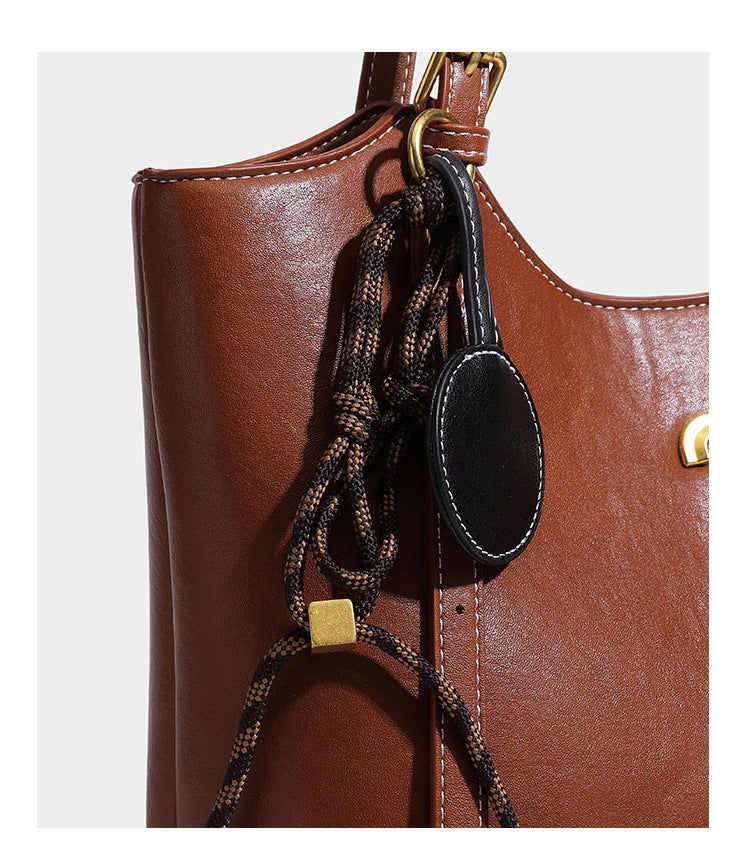 Structured smooth leather-look tote bag with long shoulder strap, gold-tone hardware, and hanging tassel-coin charm, detail