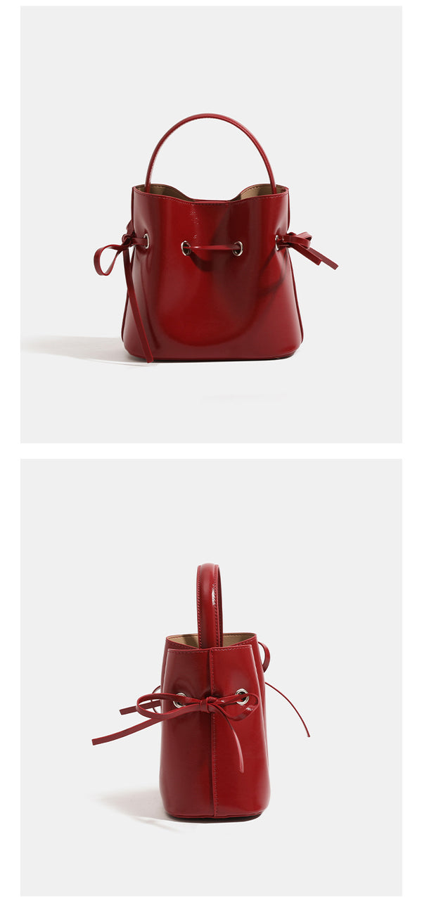 Compact glossy leather-look bucket bag with drawstring bow-tie closure, rounded top handle, and silver-tone grommet hardware
