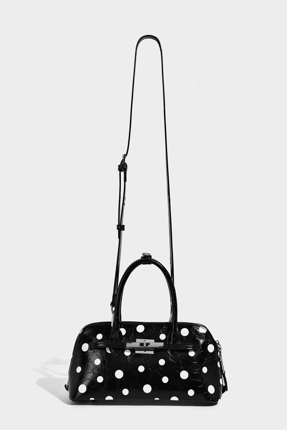 Glossy structured polka-dot satchel bag with dual top handles, silver turn-lock hardware, and detachable shoulder strap