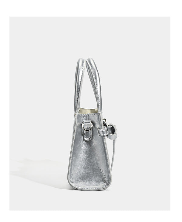 Small structured trapezoid mini top-handle bag with front belt-knot buckle detail and glossy leather-look finish, detail view