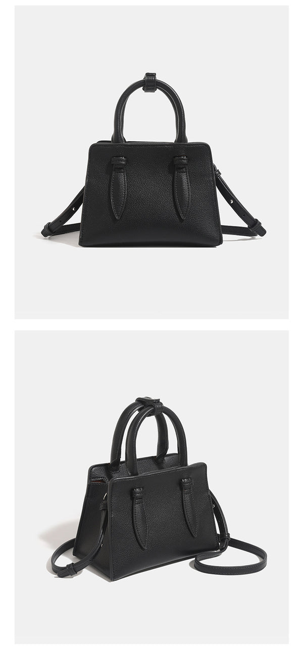 Small structured trapezoid top-handle bag in pebbled matte finish with decorative strap tabs, twin knotted handles, and