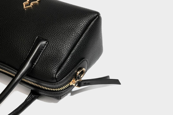 Small structured pillow satchel bag with pebbled leather-look finish, dual rolled top handles, gold-tone gourd emblem, and