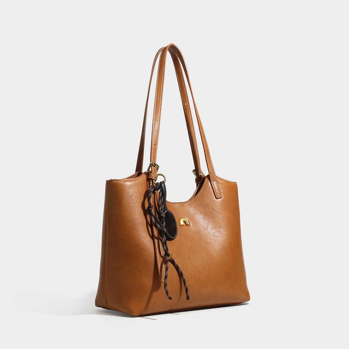 Structured smooth leather-look tote bag with long shoulder strap, gold-tone hardware, and hanging tassel-coin charm, detail