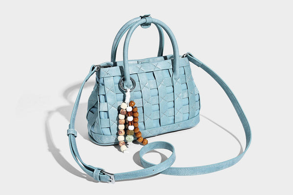 Small structured woven satchel tote with rounded top handles, silver-tone ring hardware, and bead tassel charm, detail view