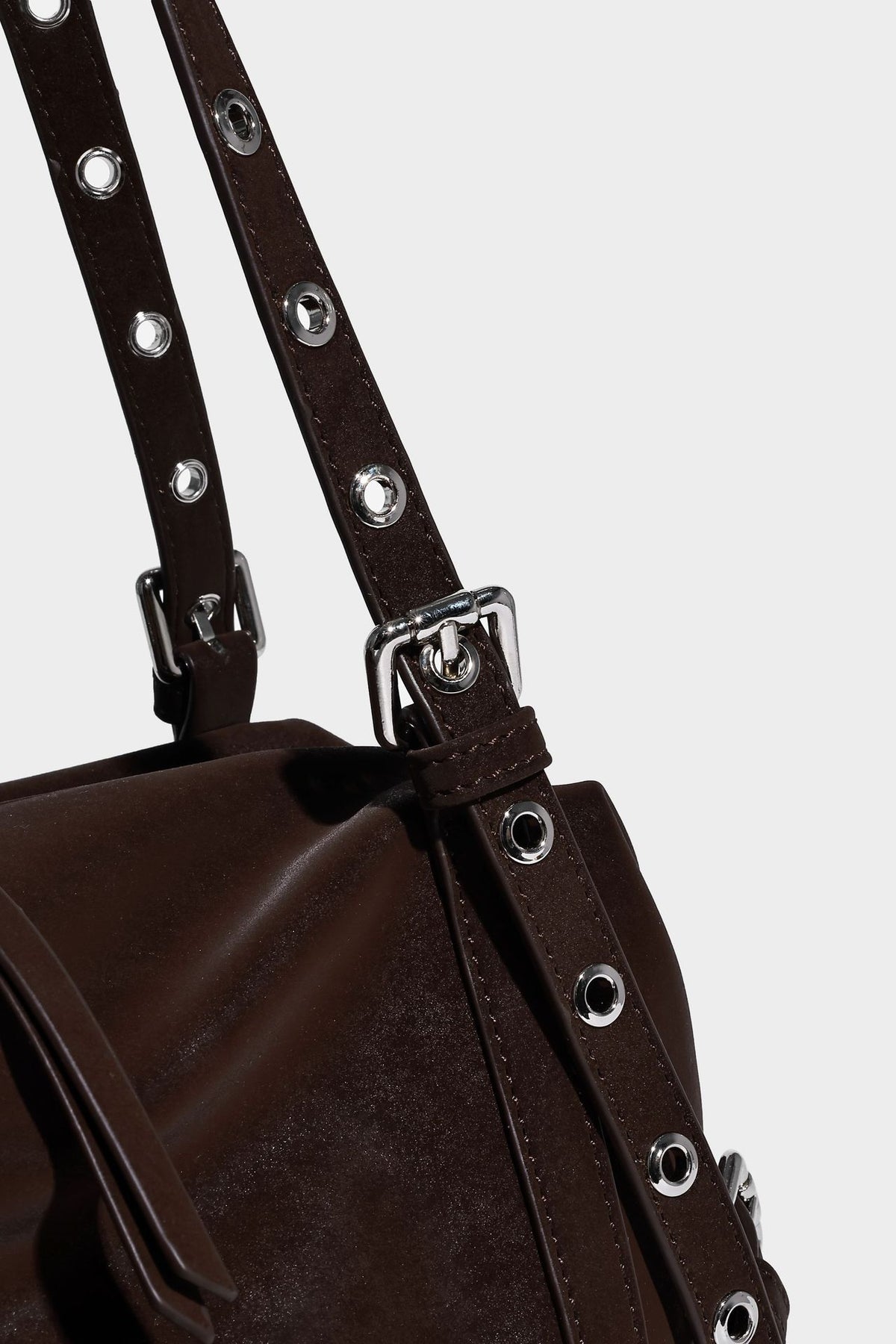 Weiche, zylinderförmige Schultertasche in Dunkelbraun mit silberfarbenen Riemen mit Ösen, Reißverschluss oben, seitlichen Schnallenbeschlägen und Quaste