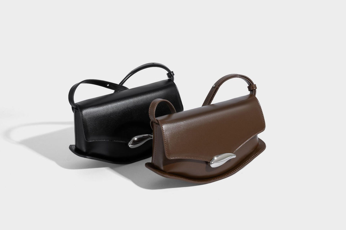 Small structured saddle bag with glossy leather-look finish, angular flap front, silver-tone metal clasp, and slim