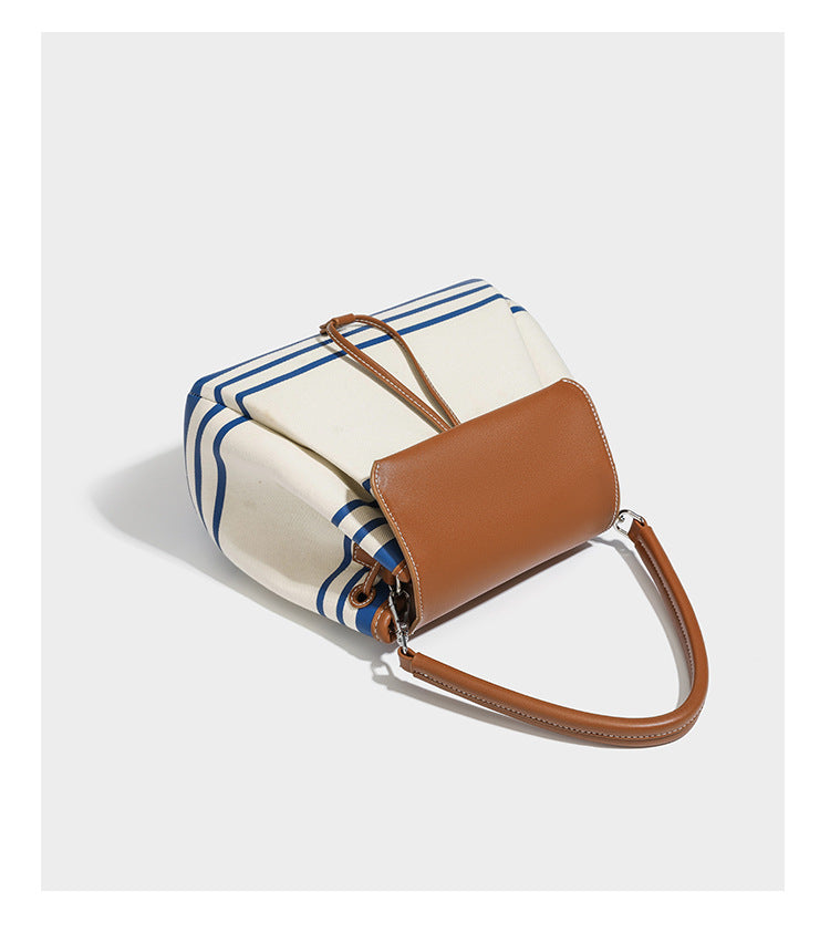 Cream canvas bucket bag with blue horizontal stripes, tan leather-look flap and trim, drawstring closure, silver-tone, detail