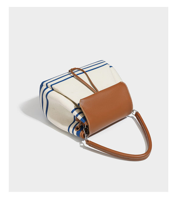 Cream canvas bucket bag with blue horizontal stripes, tan leather-look flap and trim, drawstring closure, silver-tone, detail