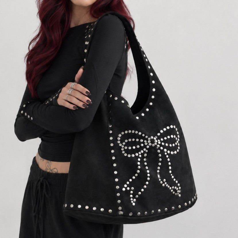 Oversized black suede-look hobo shoulder bag with silver dome studs and a large studded bow motif on the front panel, detail