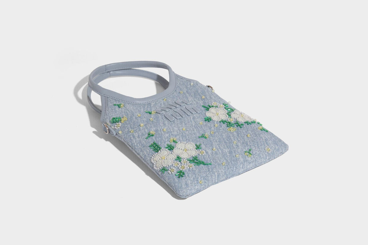 Kleine hellblaue Mini-Tote-Bag aus Stoff mit weißer Perlenblumenverzierung, runden Henkeln, silberfarbenen Beschlägen und