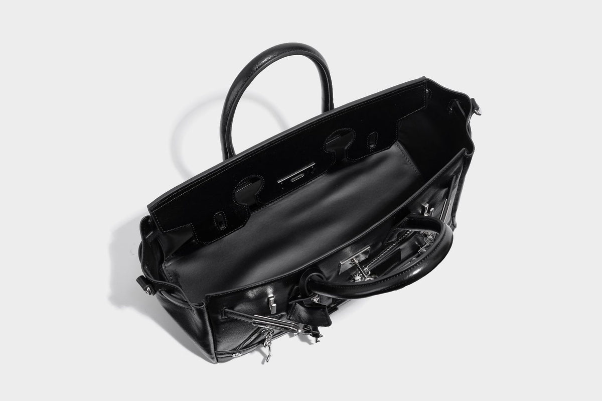 Structured black leather-look satchel bag with silver padlock hardware, front zip pockets, key charms, and top handles