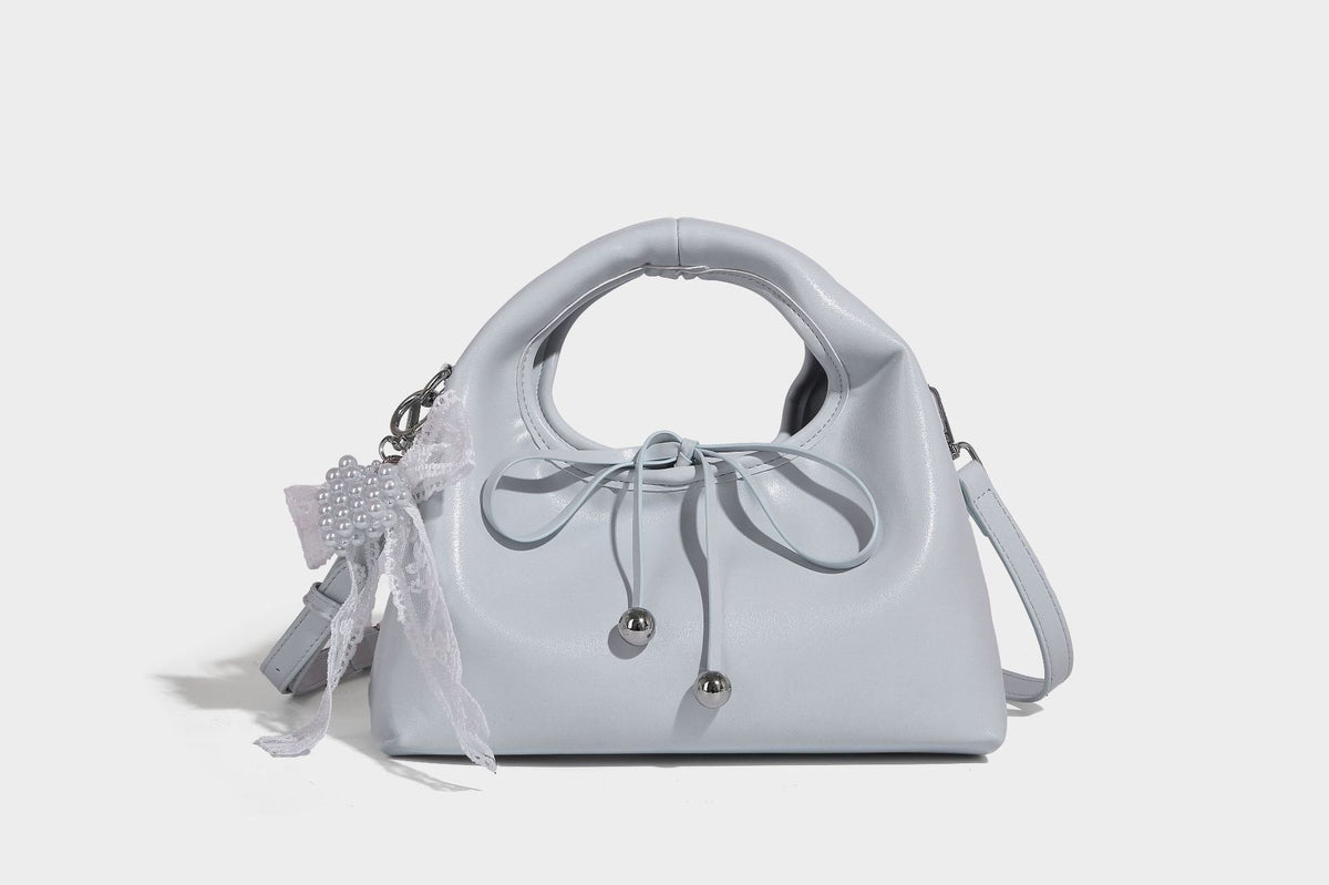Kleine kuppelförmige Henkeltasche in glänzender Lederoptik mit Kordelzugverschluss, weißem Spitzen-Schleifenanhänger und silberfarbenen Metallbeschlägen