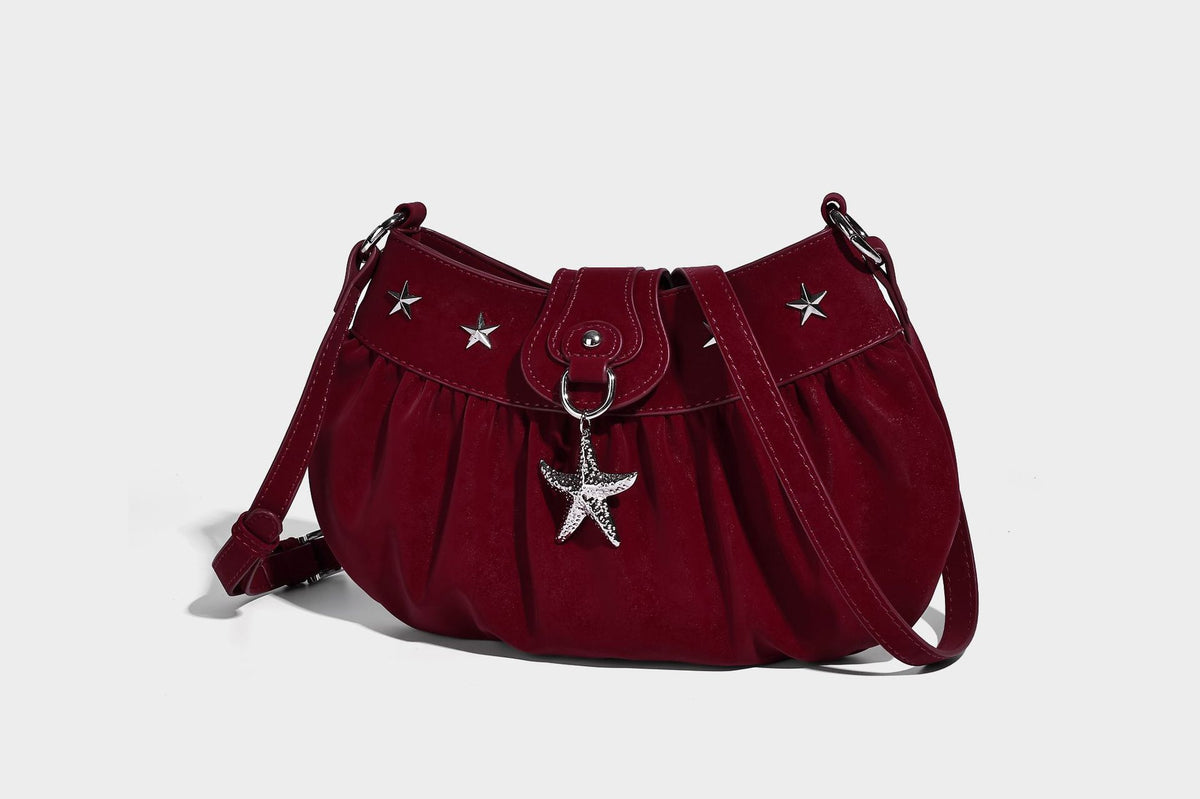 Ruched shoulder bag with curved flap, silver star studs, dangling starfish charm, and adjustable crossbody strap, detail view