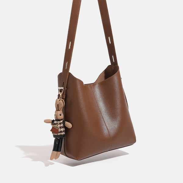Smooth leather-look bucket bag with long flat shoulder strap, open top, gold-tone hardware, and decorative rabbit charm