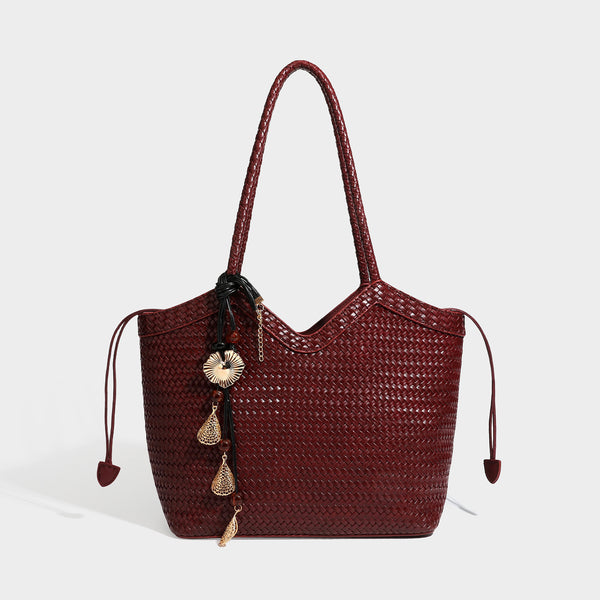 Olivgrüne Tote-Bag in Korbgeflecht-Optik mit dunkelbraunen geflochtenen Schulterriemen, seitlichen Zugbändern und Perlenanhänger in Goldoptik