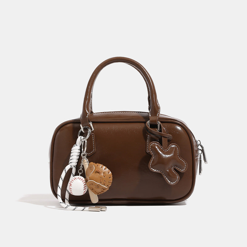 Small structured bowling barrel bag in glossy leather-look finish with twin top handles, detachable shoulder strap, and