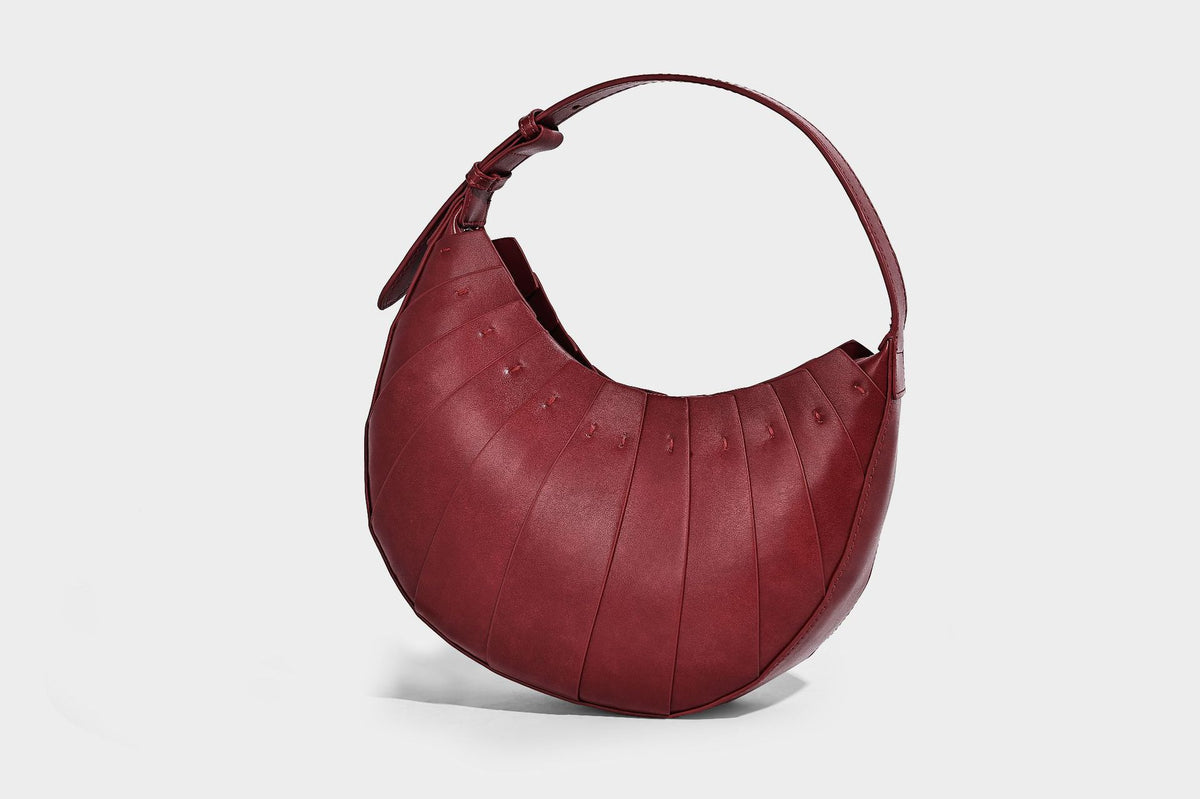 Crescent half-moon shoulder bag with vertical panel seaming, matte-satin leather-look finish, and adjustable gold-tone