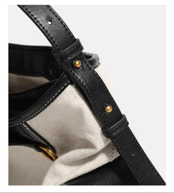 Off-white canvas hobo shoulder bag with black leather-look trim, gold-tone ring hardware, top zip closure, side pockets, and