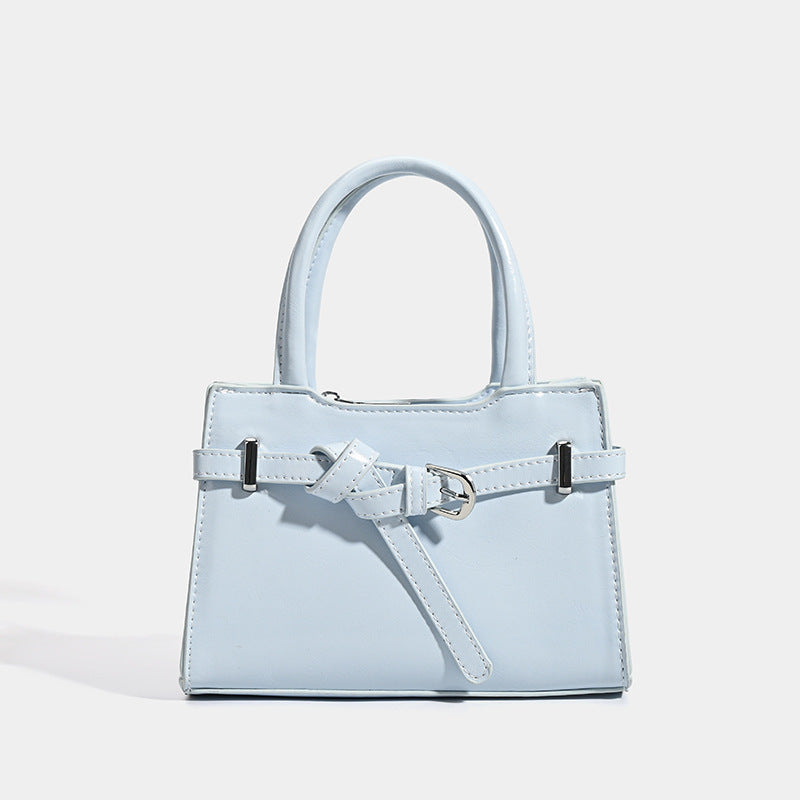 Small structured trapezoid mini top-handle bag with front belt-knot buckle detail and glossy leather-look finish, front view