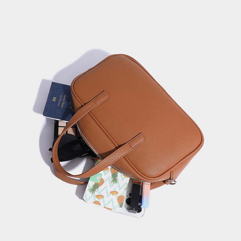 Structured pebbled leather-look Boston bowling bag in tan with blue detachable round mini pouch, dual top handles, and