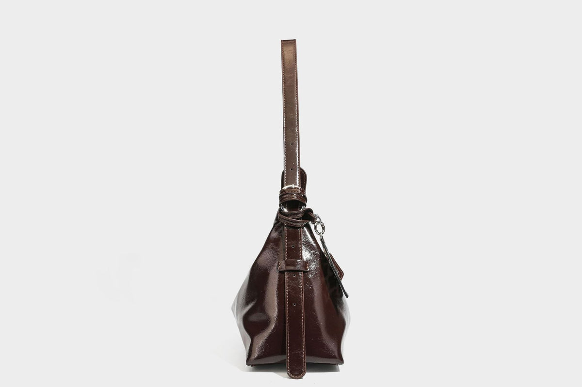 Glossy dark brown hobo shoulder bag with slim strap, front zip pocket, stud detail, and detachable leopard-print heart charm