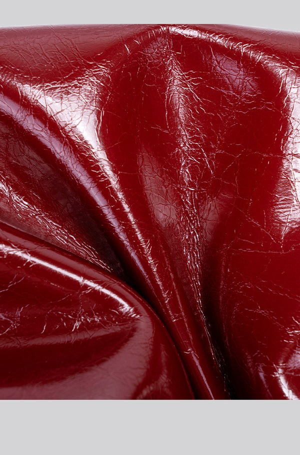 Glossy burgundy leather-look shoulder bag with curved gold-tone bar front closure, crinkled oil-wax texture, and adjustable