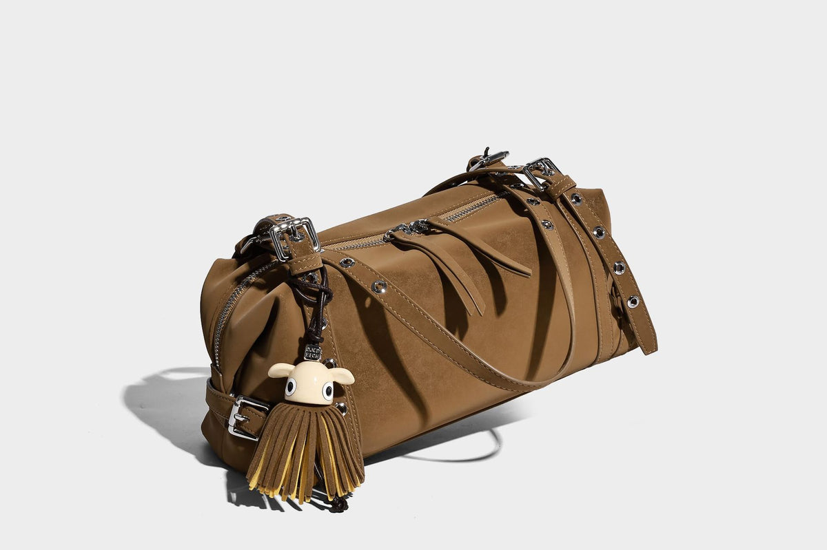 Weiche, zylinderförmige Schultertasche in Dunkelbraun mit silberfarbenen Riemen mit Ösen, Reißverschluss oben, seitlichen Schnallenbeschlägen und Quaste